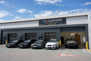 BMW Customz car customization shop with various cars parked outside on a clear day.
